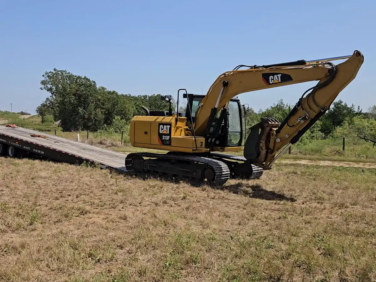 Excavator coming off the trailer onto cleared ground by the tree line